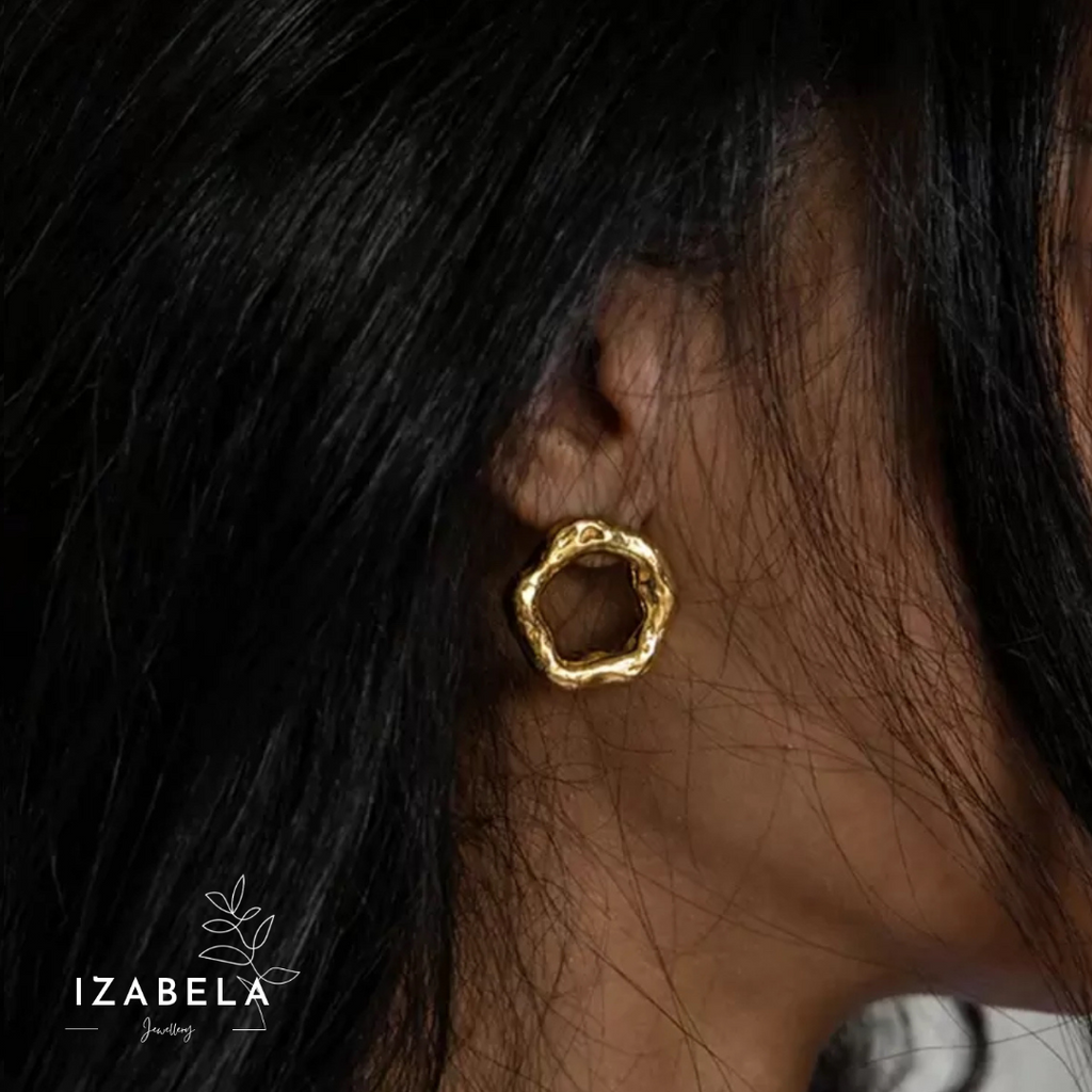 Gold earring worn by a person with dark hair, brand 'IZABELA' visible.
