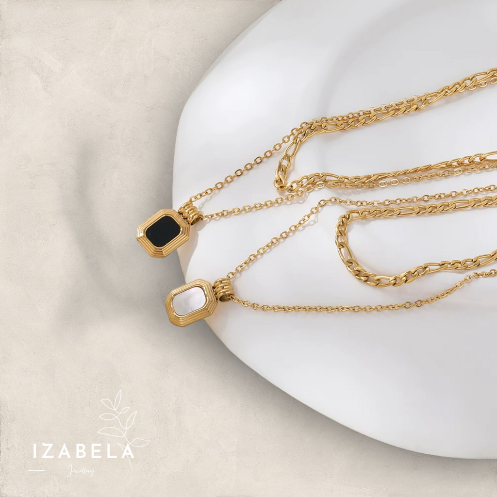 Gold necklaces with black pendants on a white plate, featuring the brand 'Izabela'.